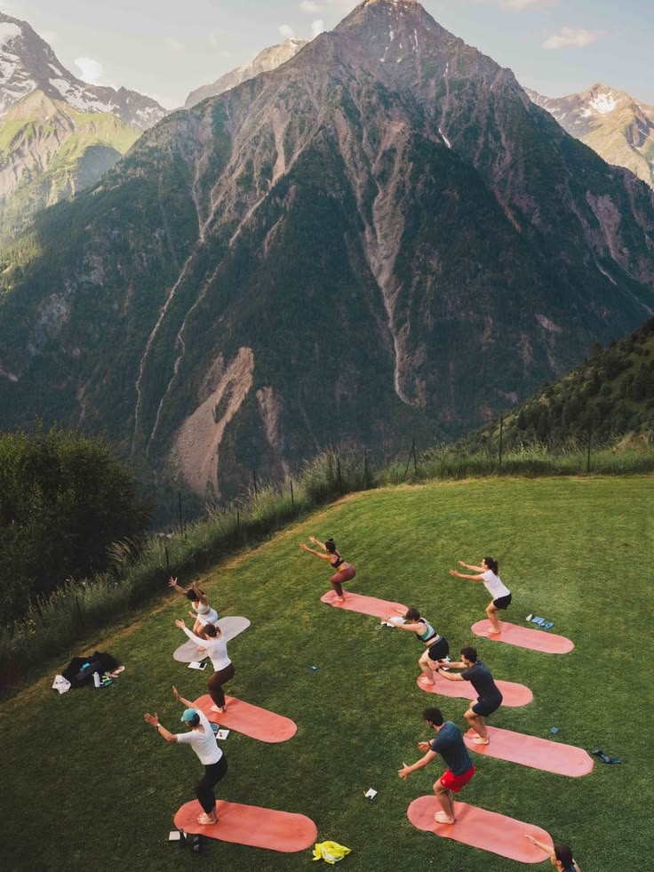 An outdoor class on clay-colored mats along a green mountain slope.